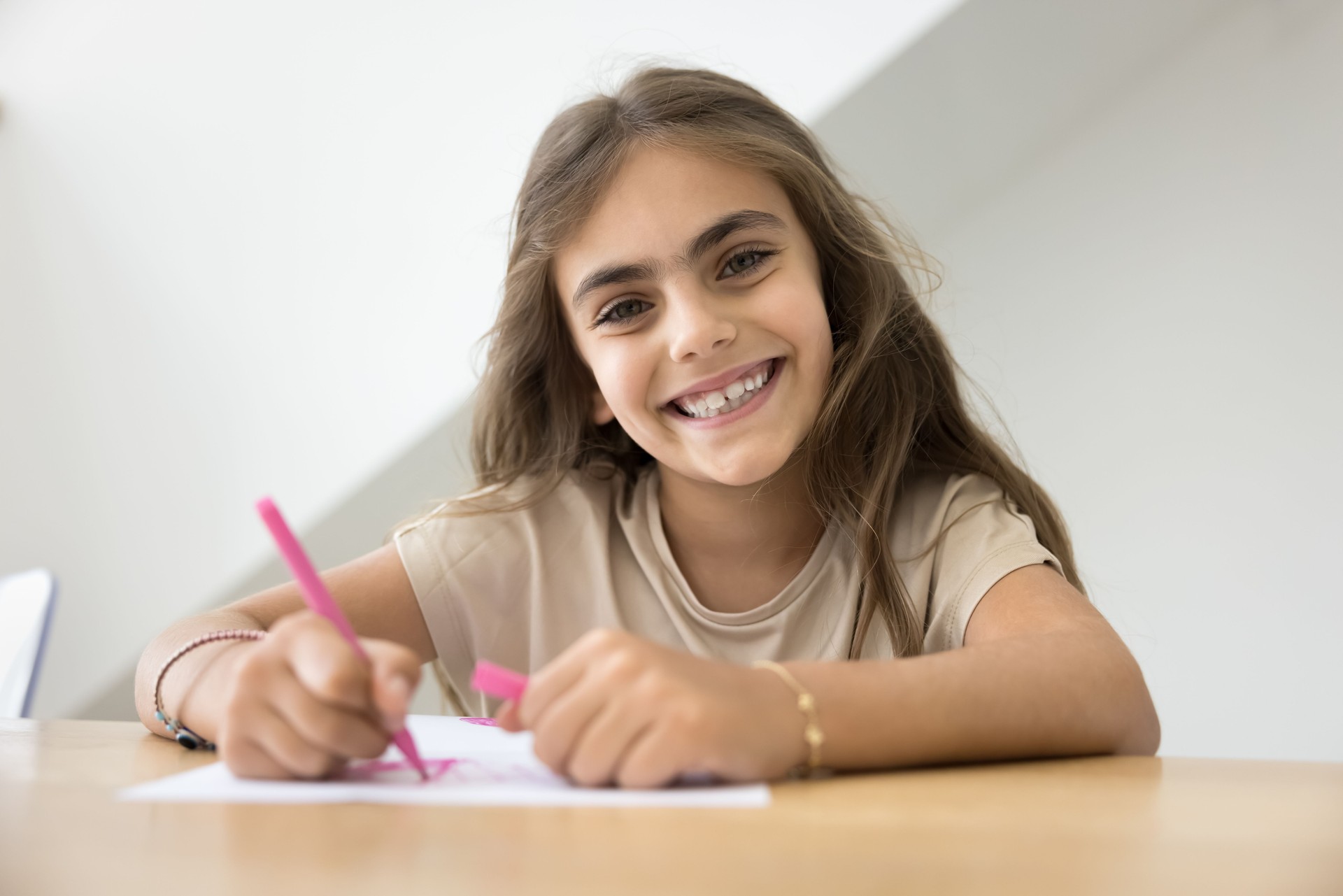 Cheerful early schoolgirl kid drawing pink sketches in colorful pencils